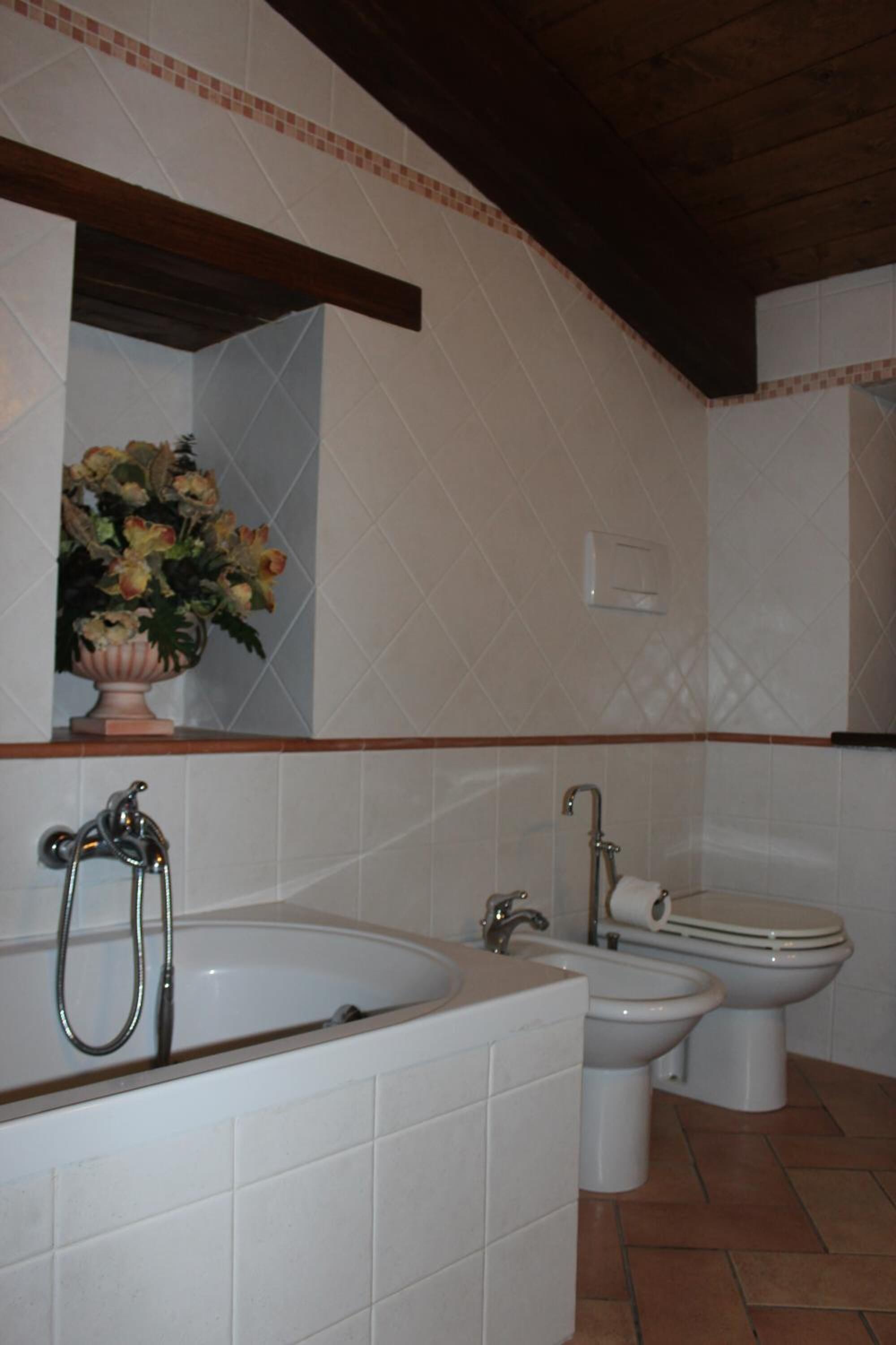 Un bany amb banyera, un lavabo i un vàter. Hi ha un ram de flors a la paret.