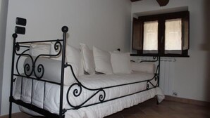 Una cama individual con estructura metálica y ropa blanca en una habitación con paredes blancas y techo de madera.