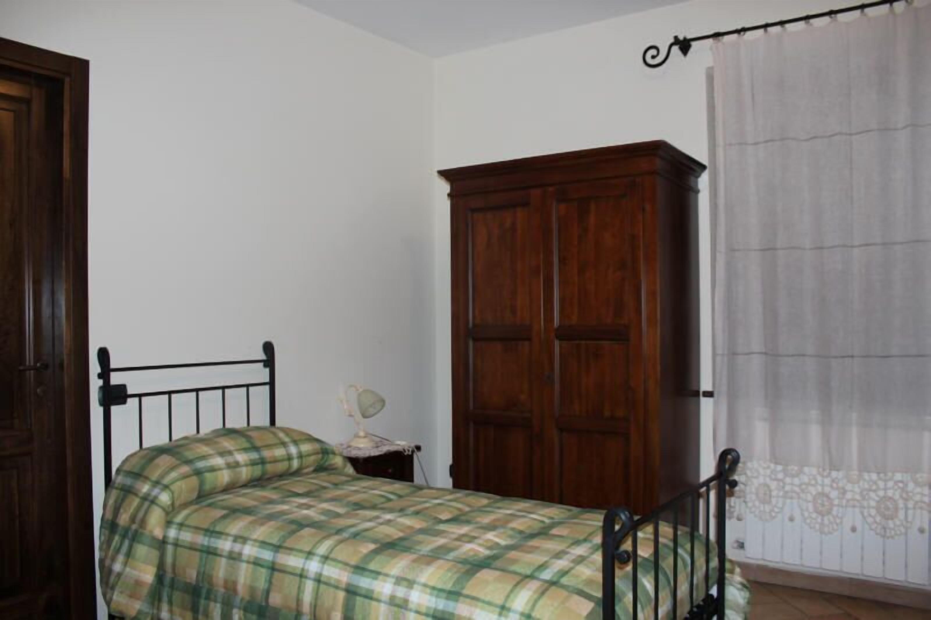 A bedroom with a bed, a wooden wardrobe, a nightstand with a lamp, and a curtain.