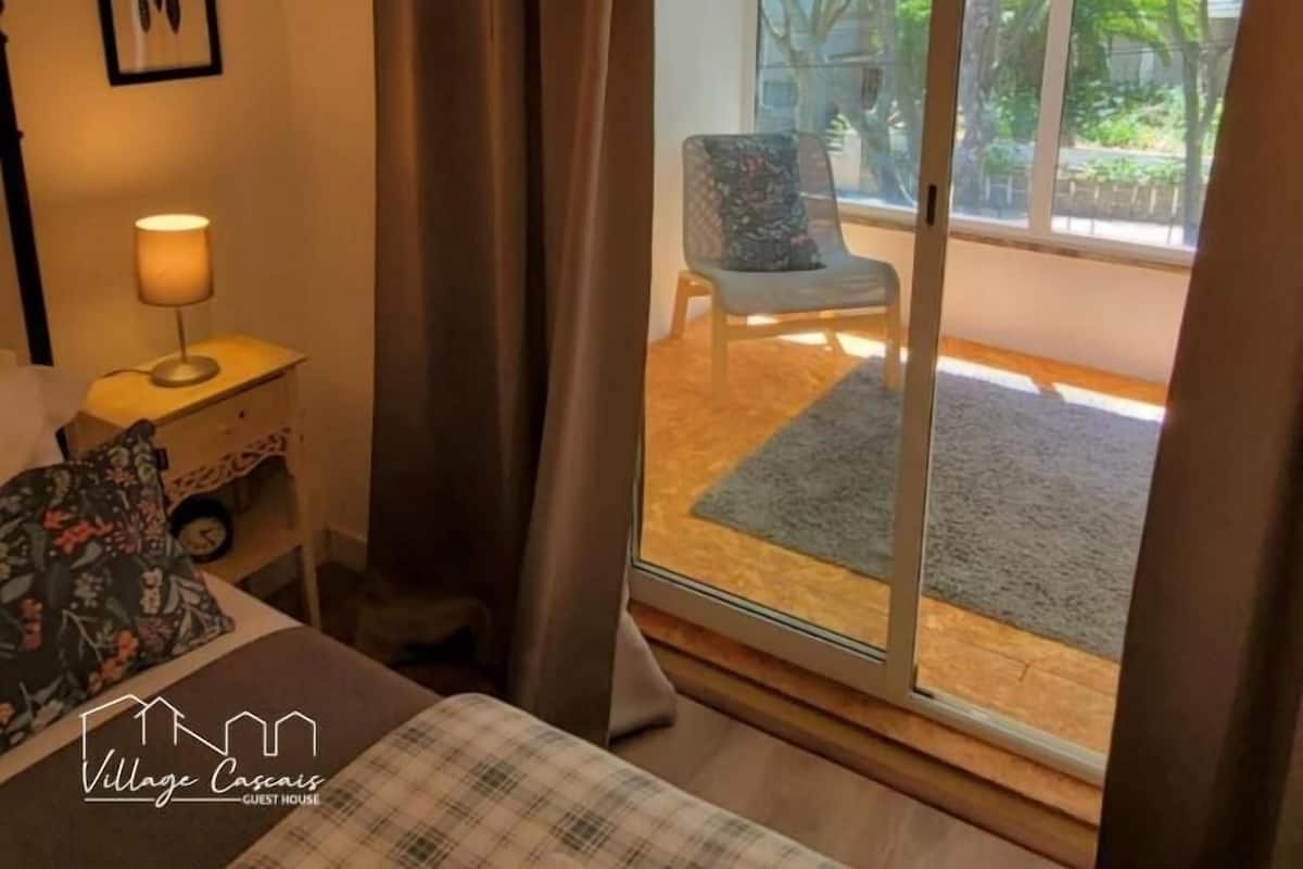 A bedroom with a bed, a nightstand with a lamp, a chair, and a view of a balcony with a door.