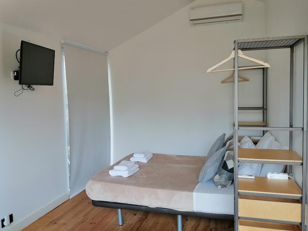 Et lille værelse med seng, fjernsyn ophængt på væggen, garderobeskab med plads til at hænge tøj og et lille bord.