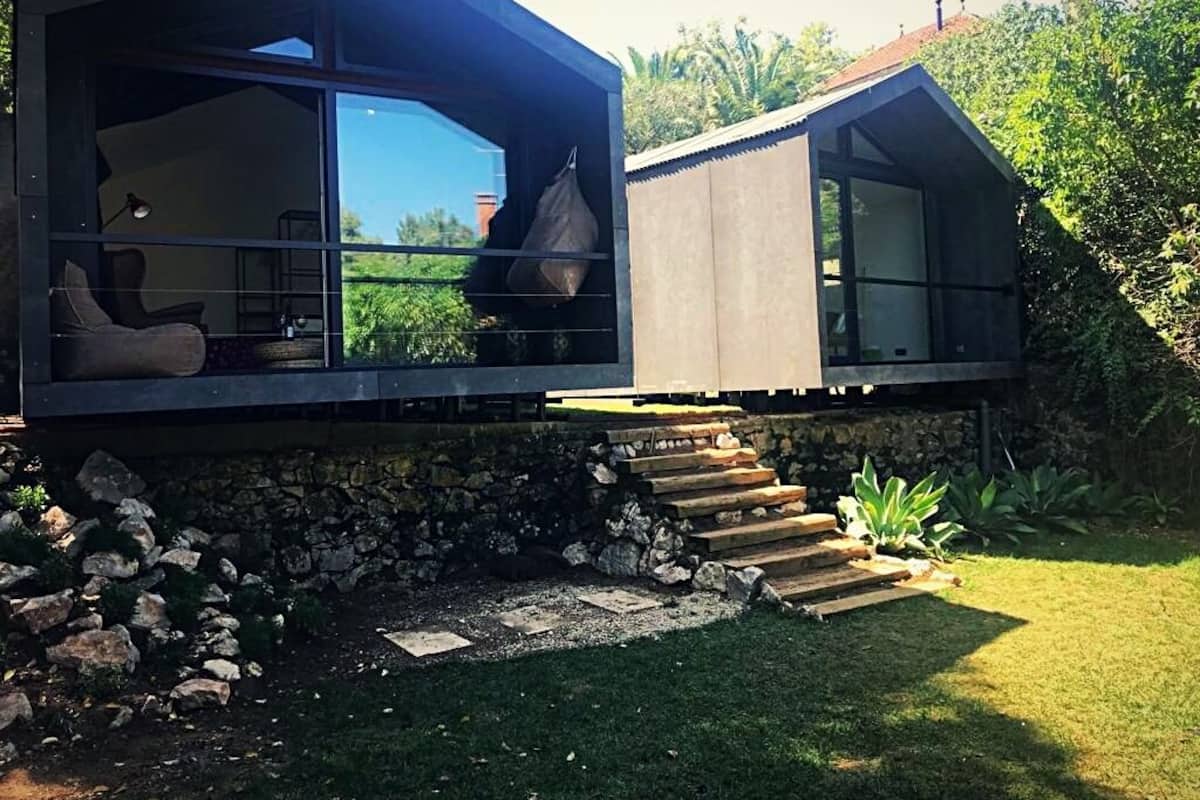 A modern house with a glass extension, stone steps, and a grassy yard.