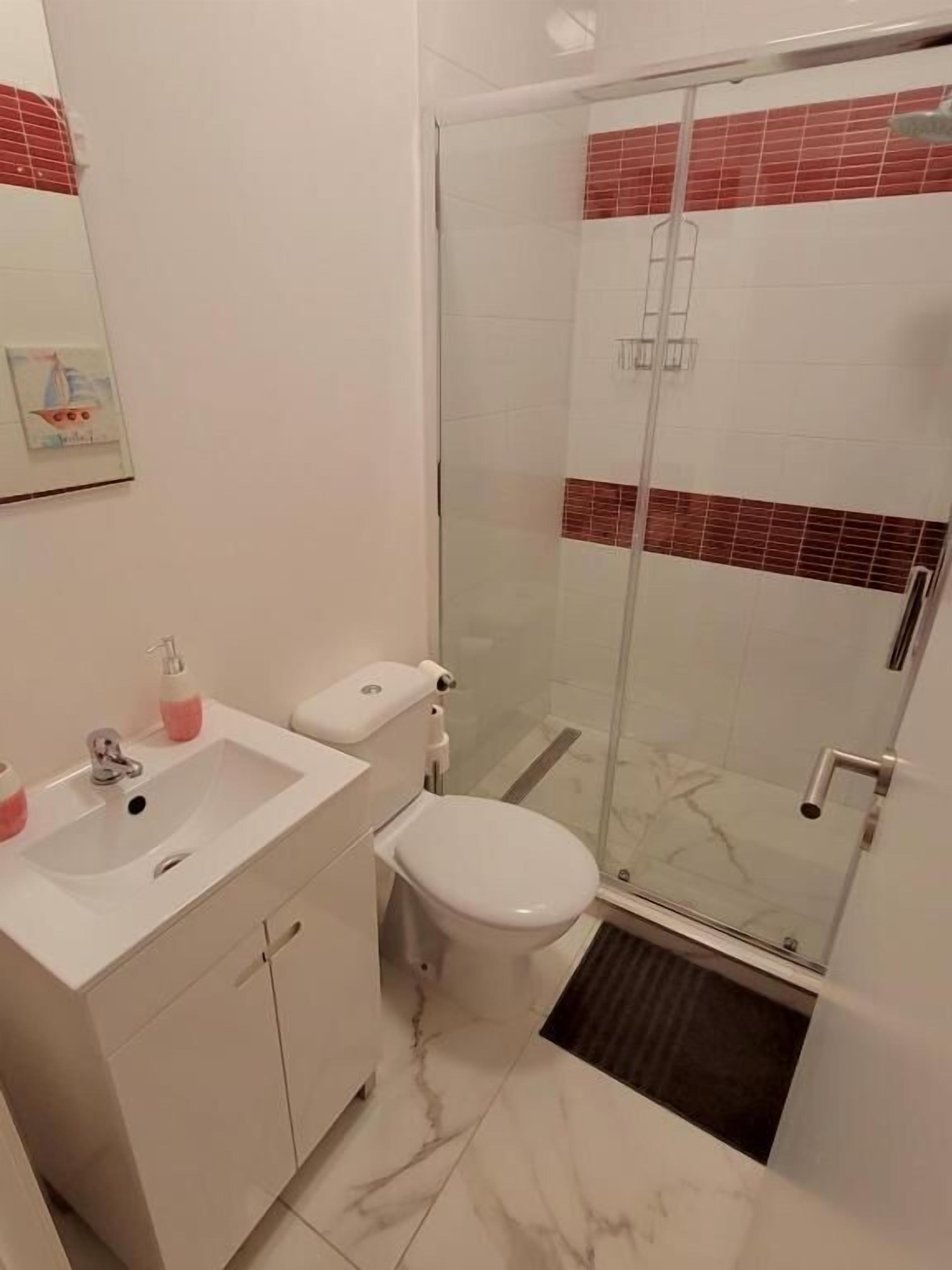 Een badkamer met een wit wastafelmeubel, toilet en een douchecabine van glas.