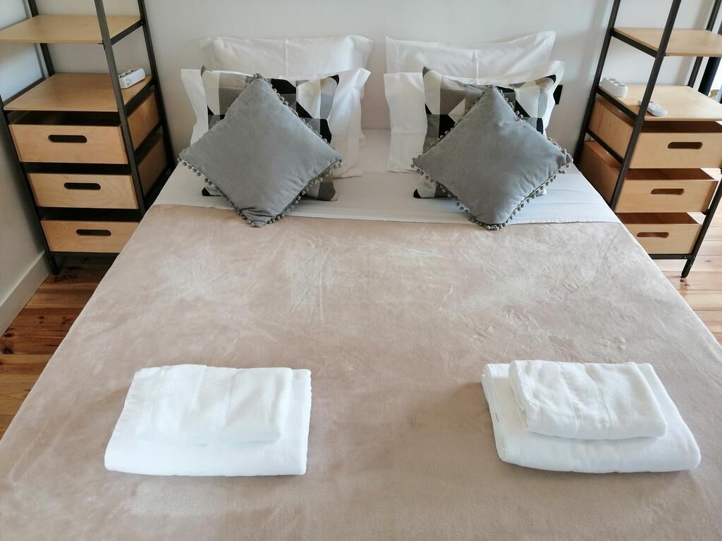 A neatly made bed with two pillows, a bedside table with a lamp, and a wooden nightstand with drawers.