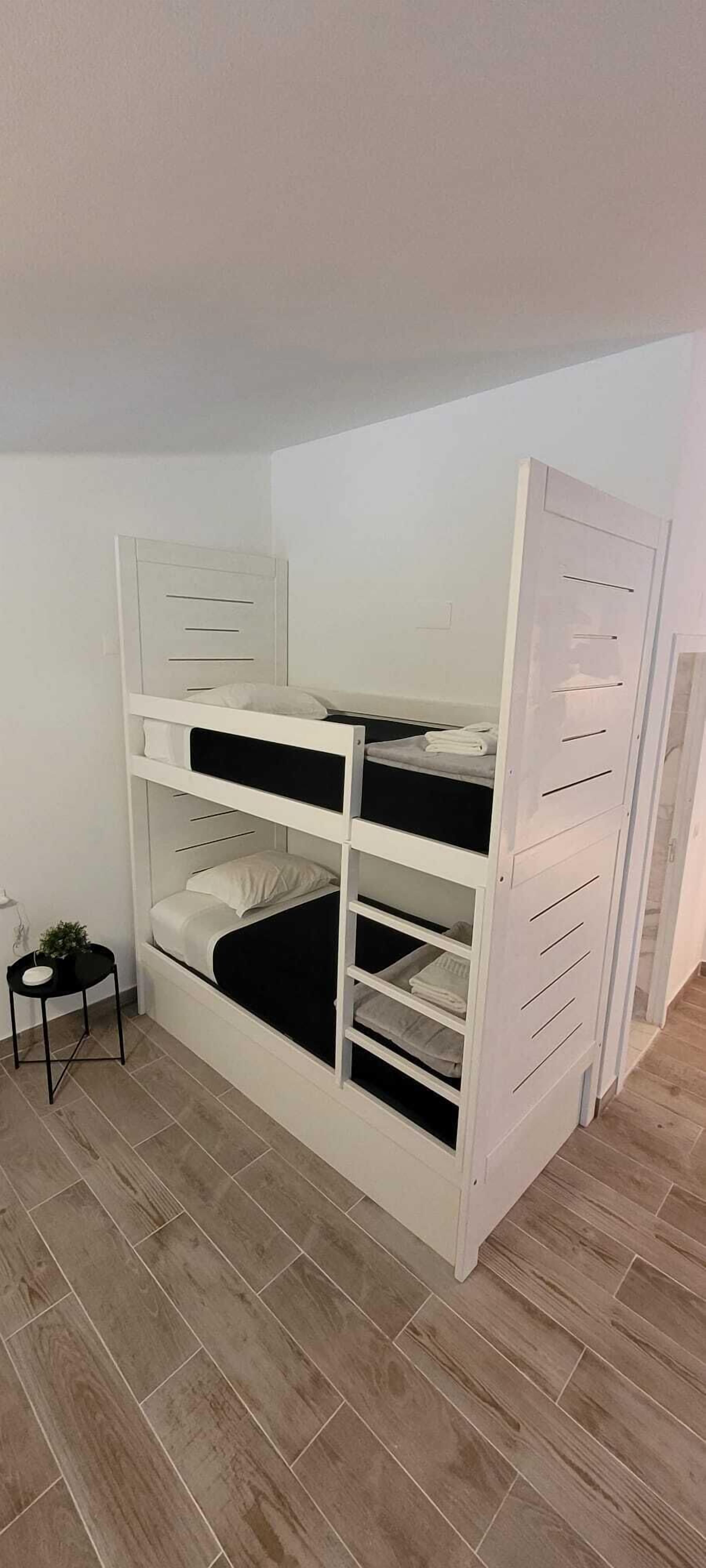 Ein Stockbett mit Stauräumen, ein kleiner Nachttisch mit einer Pflanze und ein Fliesenboden.