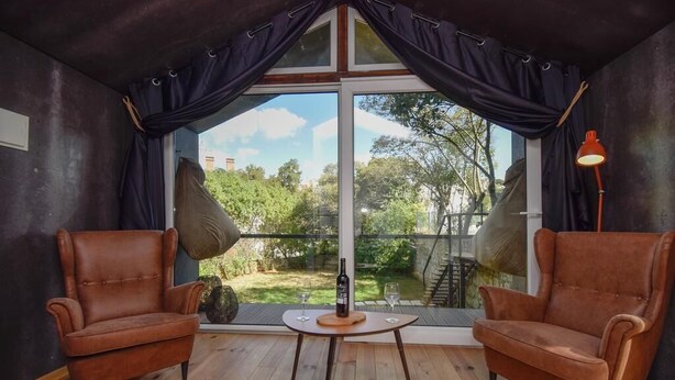A room with two leather armchairs, a small table with a bottle and glass, and a large window with curtains. - Village Cascais Guest House (Cascais)