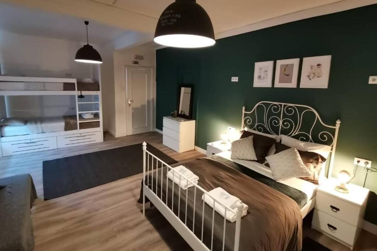 A bedroom with a bunk bed, bedside tables, a bed with a headboard, and wall art.
