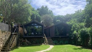 A house with a stone staircase leading to a wooden deck, surrounded by lush greenery. - Village Cascais Guest House (Cascais)