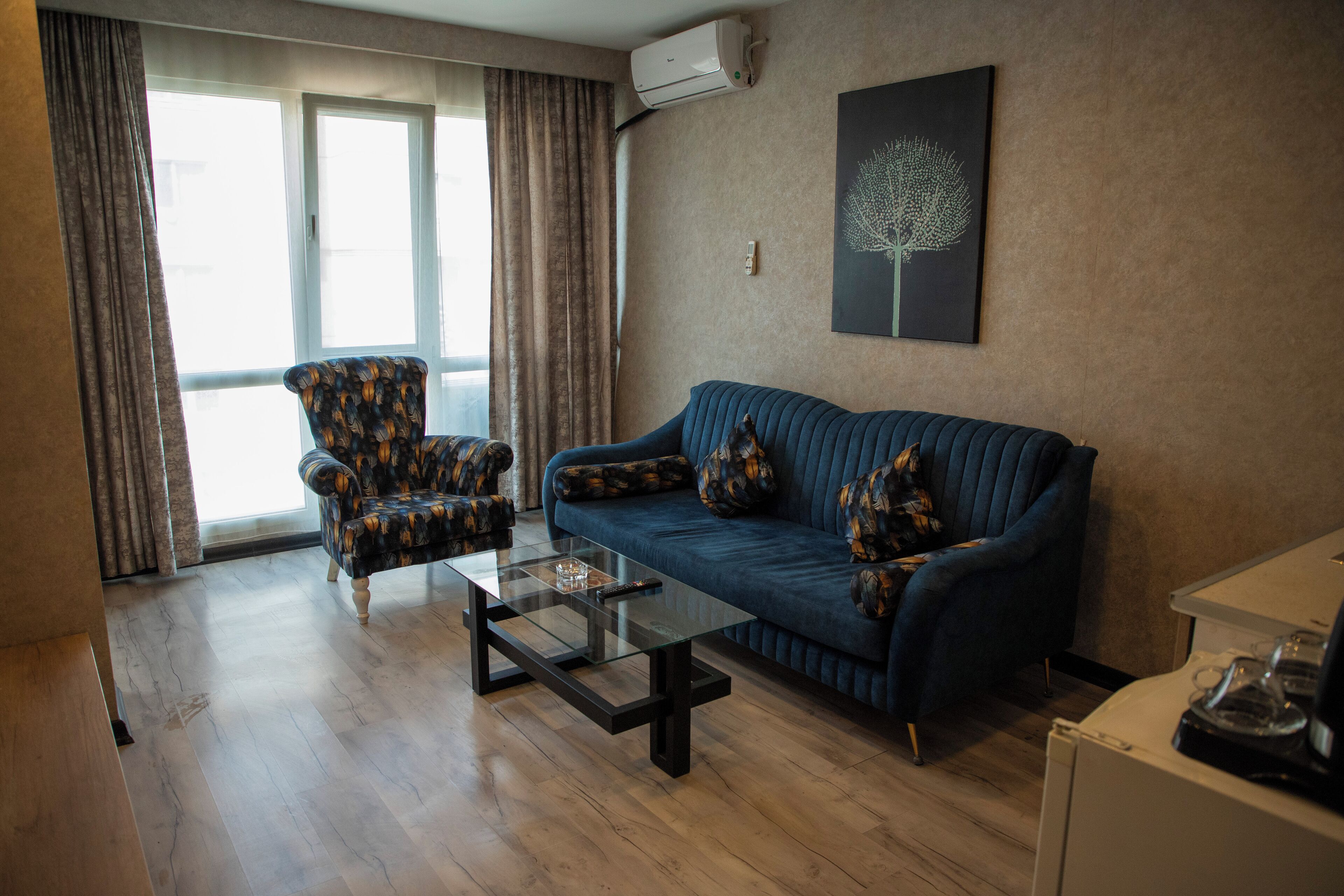 A living room with a sofa, armchair, and coffee table, a window with curtains, and an air conditioning unit.