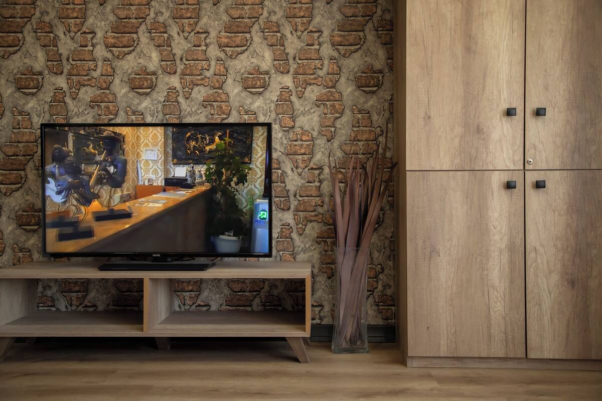 A television on a wooden stand against a brick wall, with a wooden cabinet to the right.