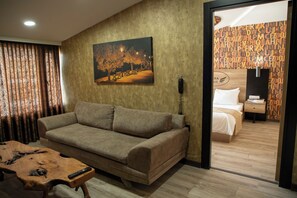 A hotel room with a sofa, a painting of a park scene, a wooden coffee table, and a bed with a nightstand. - Hera Suite Ataşehir (Istanbul)