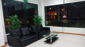 A modern living room with a black leather sofa, a glass coffee table, and two potted plants. - Blue Orchids Hotel (Hat Yai)