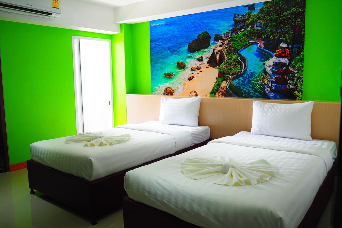 A hotel room with two beds, a green wall, and a large window.