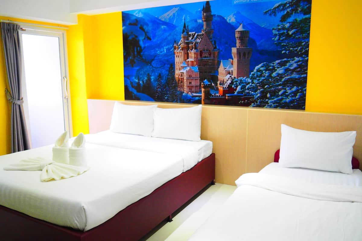 A hotel room with a large bed, a smaller bed, and a poster of a castle on the wall.