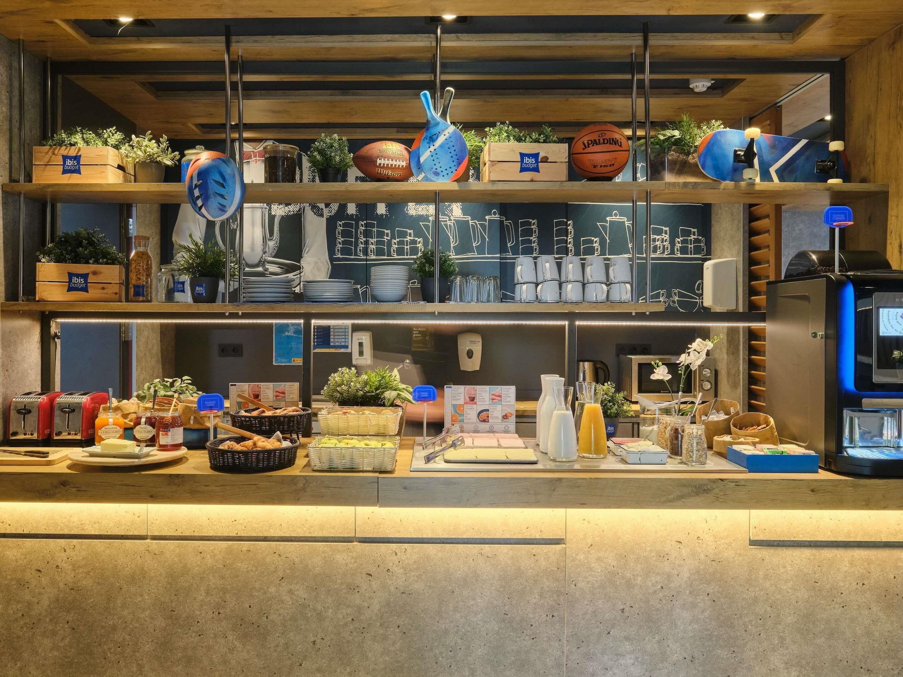 A hotel reception area with a wooden counter, various food items, a coffee machine, and decorative items like a football and a skateboard.