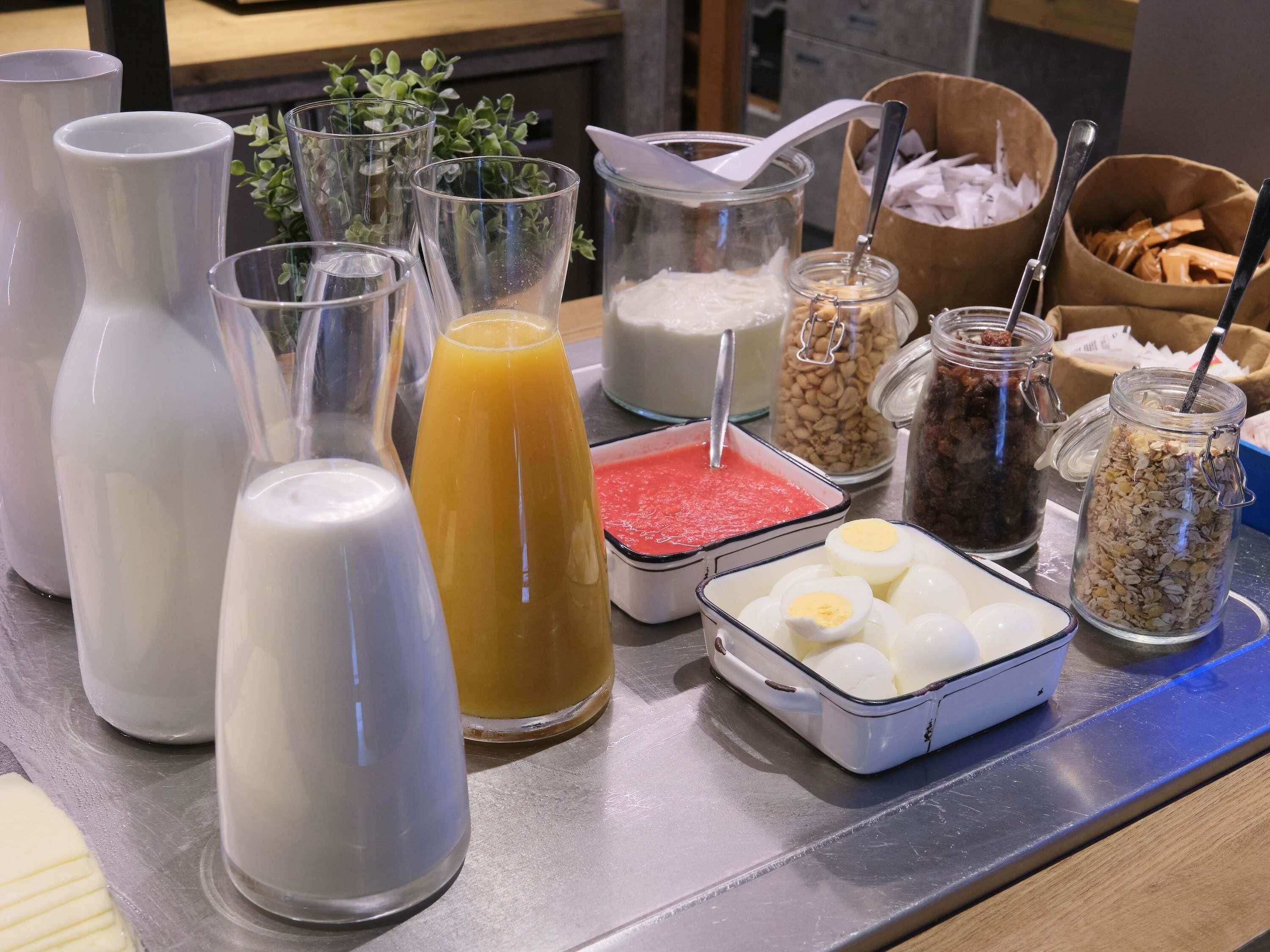 Una barra de desayuno con diversas bebidas y alimentos, entre ellos leche, zumo de naranja y un batido rojo.