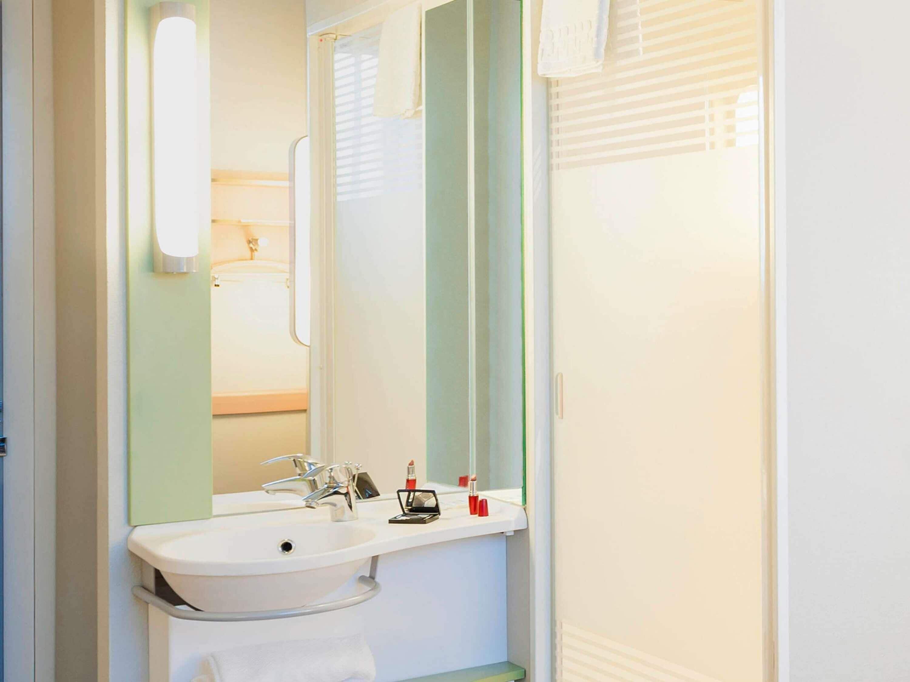 Une salle de bain avec un lavabo blanc, un miroir et une serviette accrochée au mur.