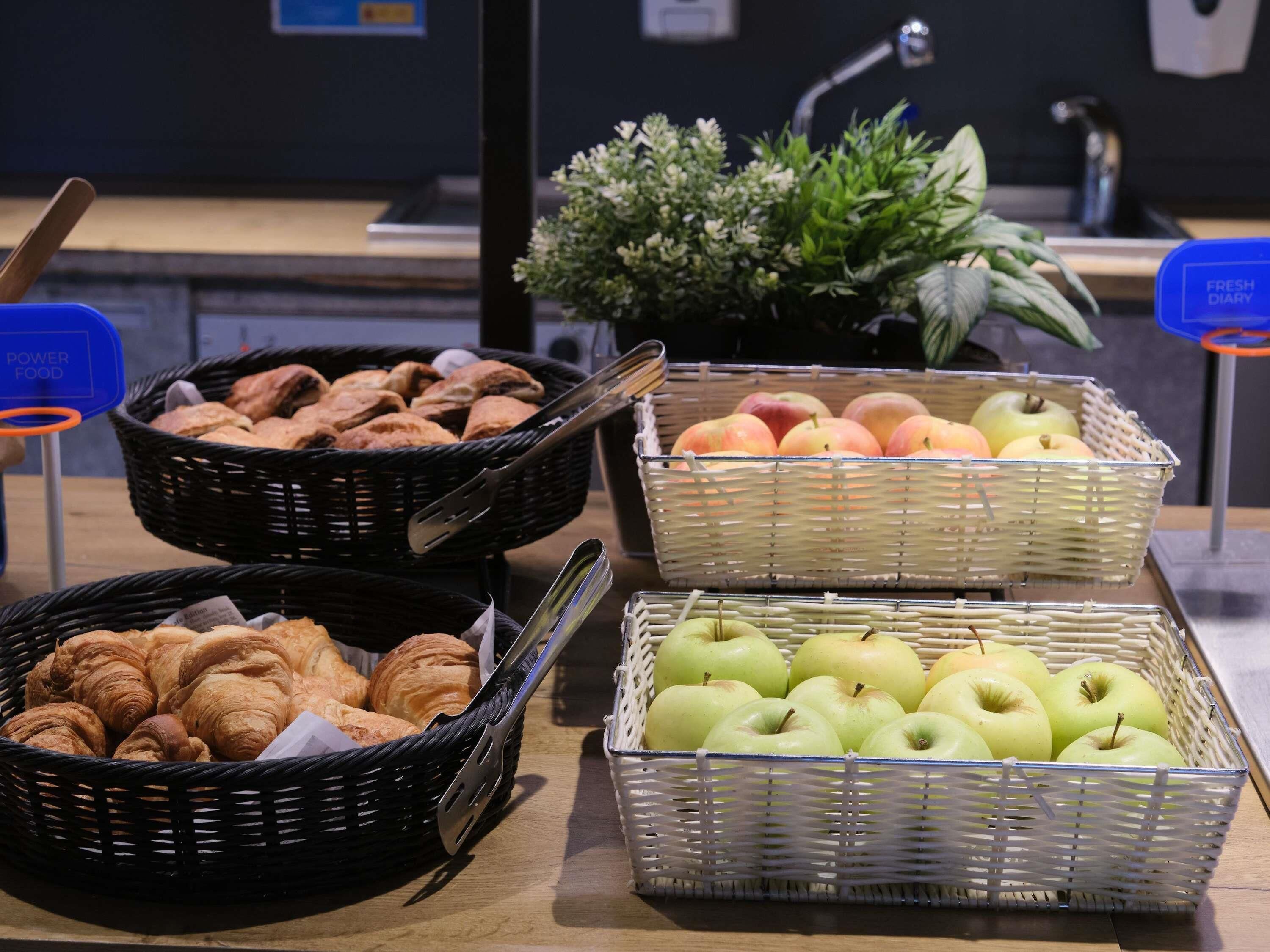 A buffet table with baskets of croissants, peaches, and green apples.
