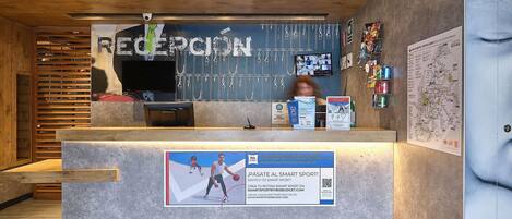 A reception area with a wooden ceiling, a reception desk, a wall-mounted TV, and a poster advertising a sports program.