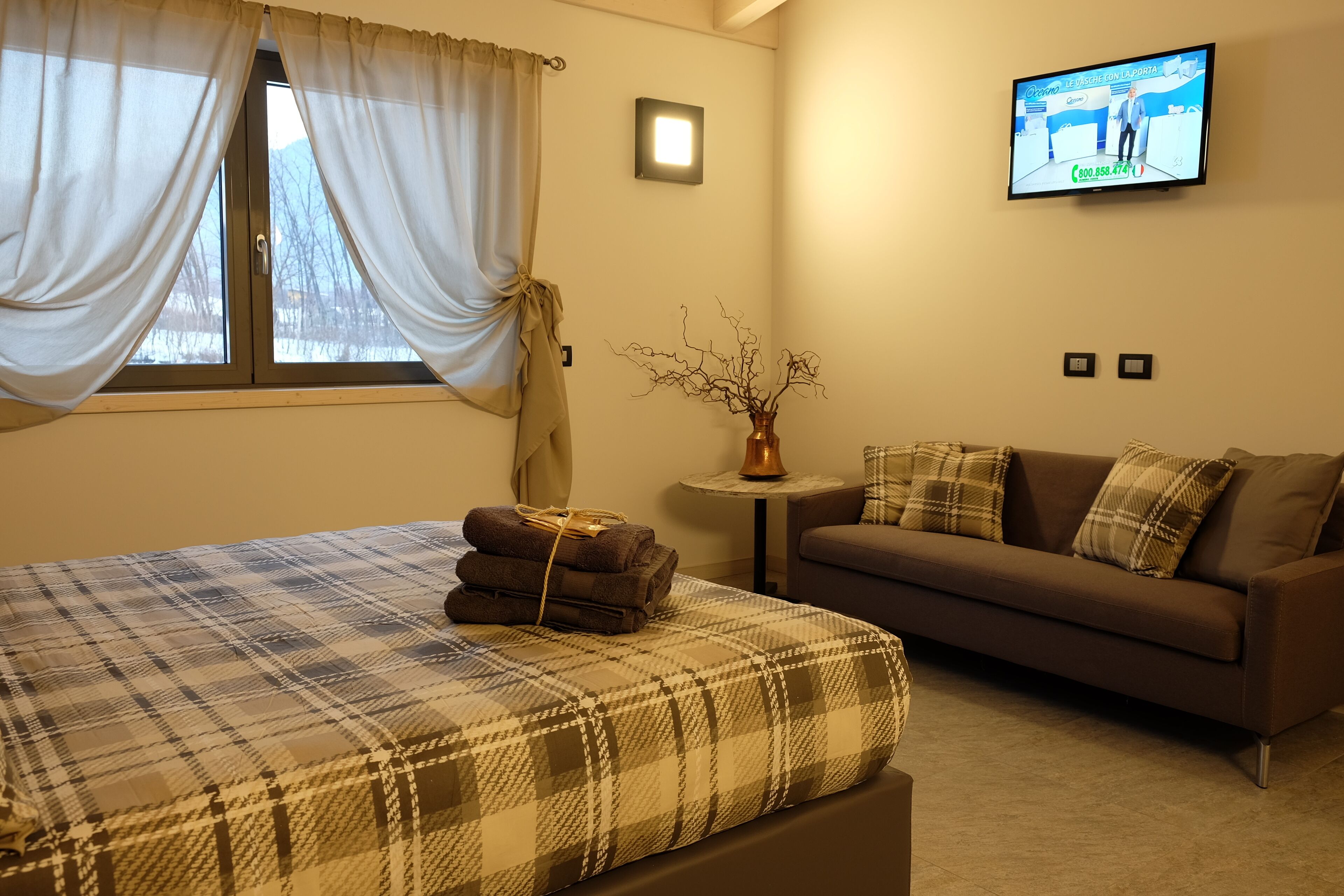 A bedroom with a bed, a sofa, a TV, and a window with curtains.