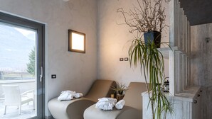 A modern spa room with two curved seating areas, a large window, and a potted plant. - Arbulé Agriturismo & Spa Valtellina (Poggiridenti)