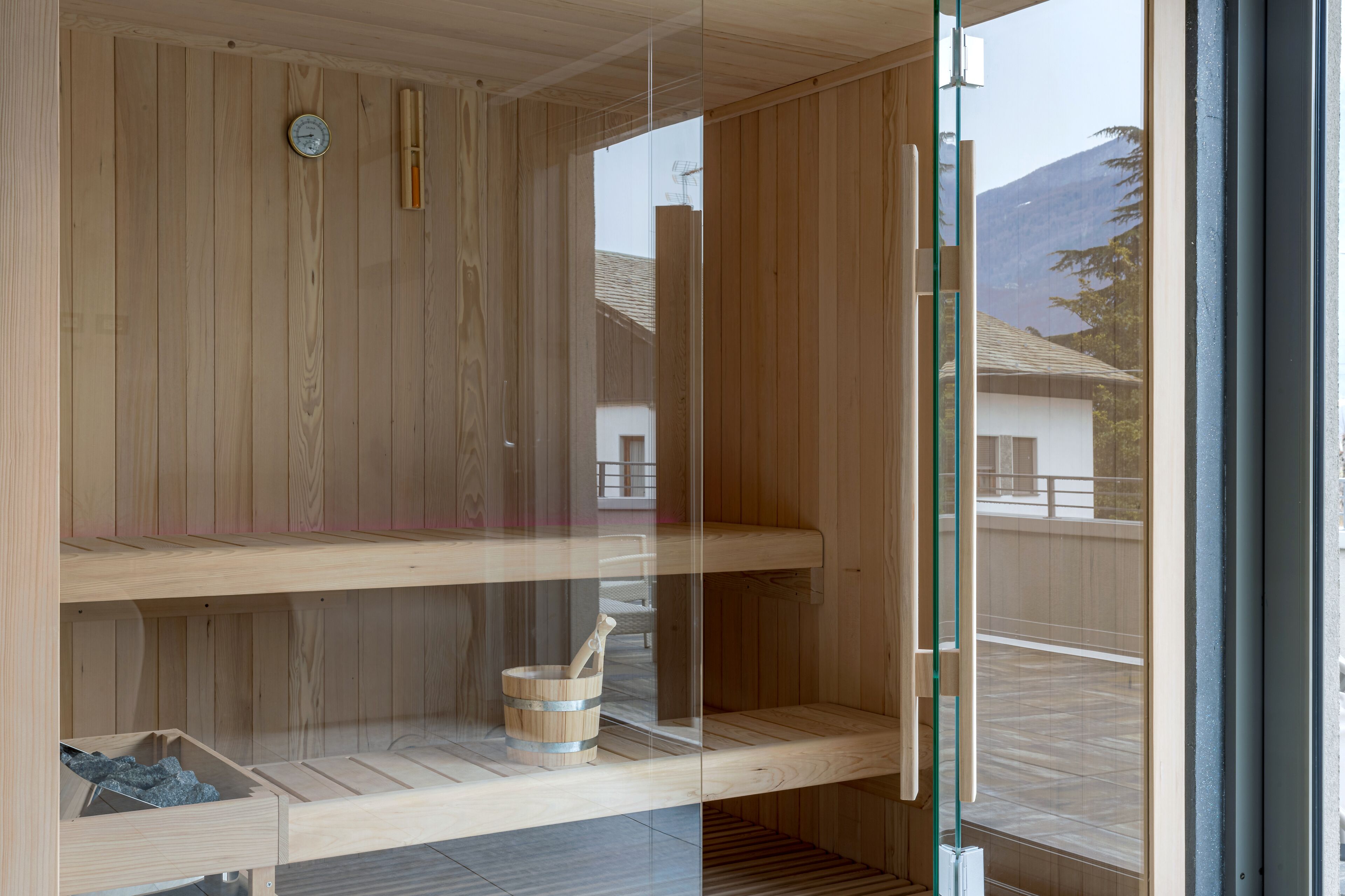 A wooden sauna with a glass door, a wooden bench, and a stone basin.