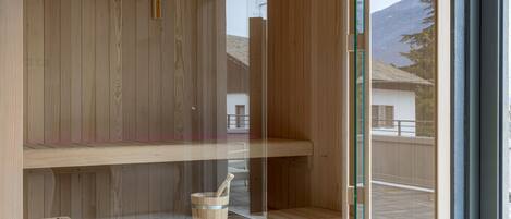 A wooden sauna with a glass door, a wooden bench, and a stone basin.