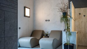 A modern waiting area with two cushioned chairs, a potted plant, and a light fixture on the wall. - Arbulé Agriturismo & Spa Valtellina (Poggiridenti)