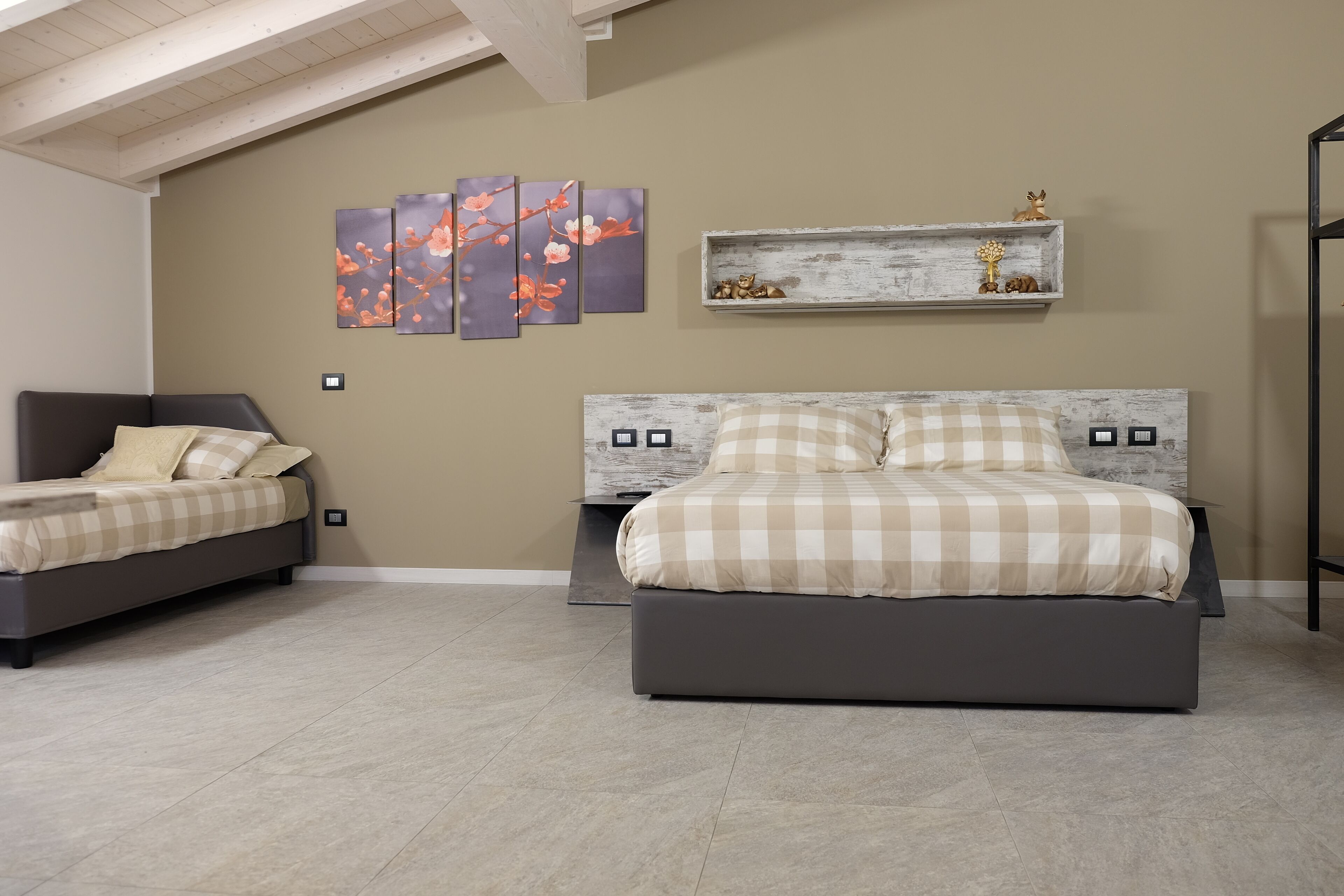 A bedroom with a large bed, a smaller sofa, and a wall-mounted shelf with decorative items.