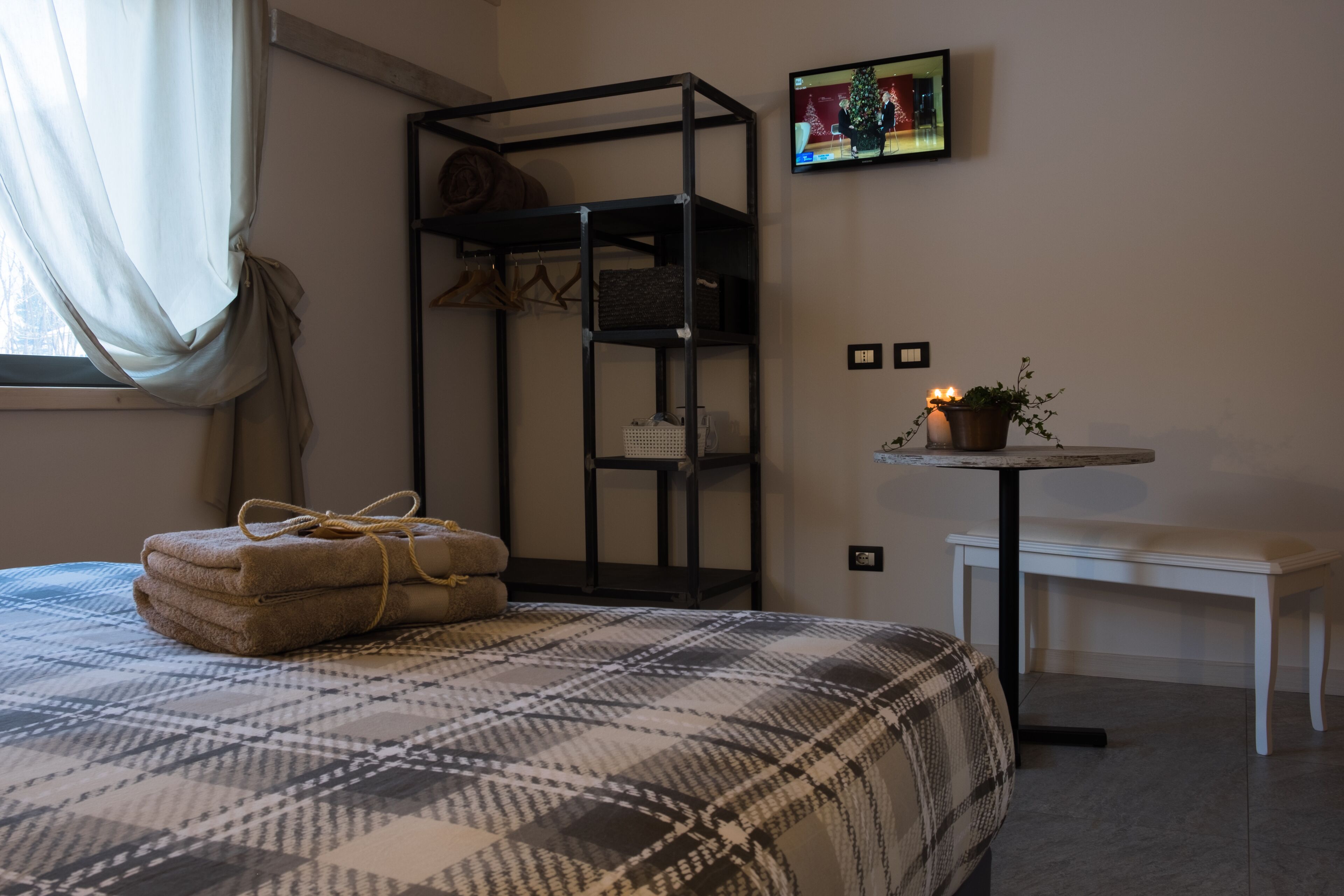 A neatly arranged bedroom with a bed, a small table with a plant, a bench, and a wall-mounted TV.