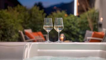 Two glasses of white wine on a white table with a view of greenery and mountains in the background.