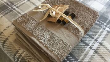 Une serviette pliée, ornée d’un motif texturé, nouée avec un ruban et accompagnée de deux petits flacons, le tout posé sur une surface en tissu à motifs.