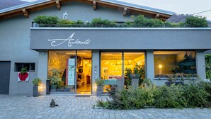 A modern building with a balcony, a sign reading "Austulé," and a welcoming entrance with plants and a bench outside. - Arbulé Agriturismo & Spa Valtellina (Poggiridenti)