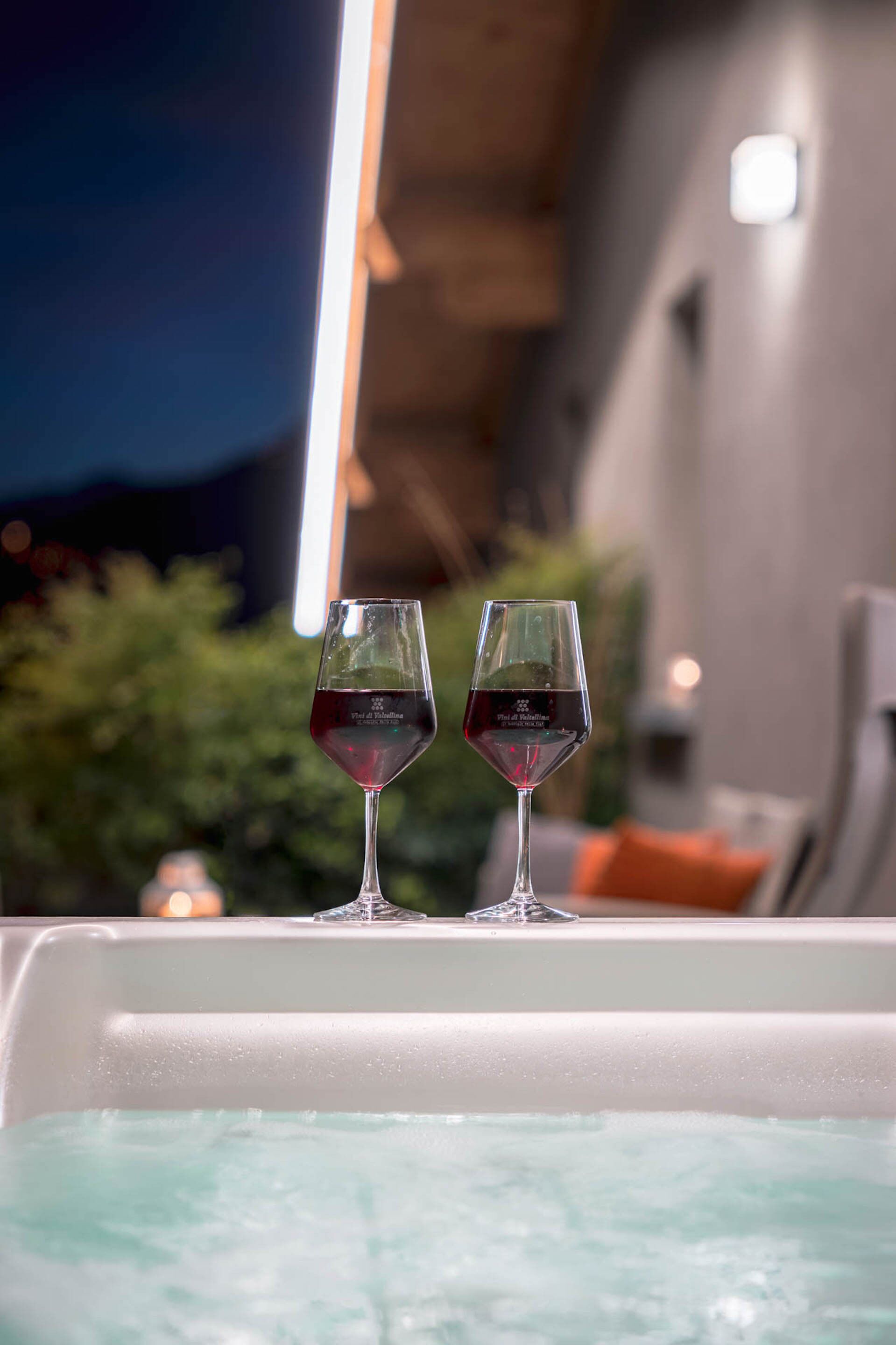 Duas taças de vinho tinto numa borda de banheira com um fundo exterior desfocado.
