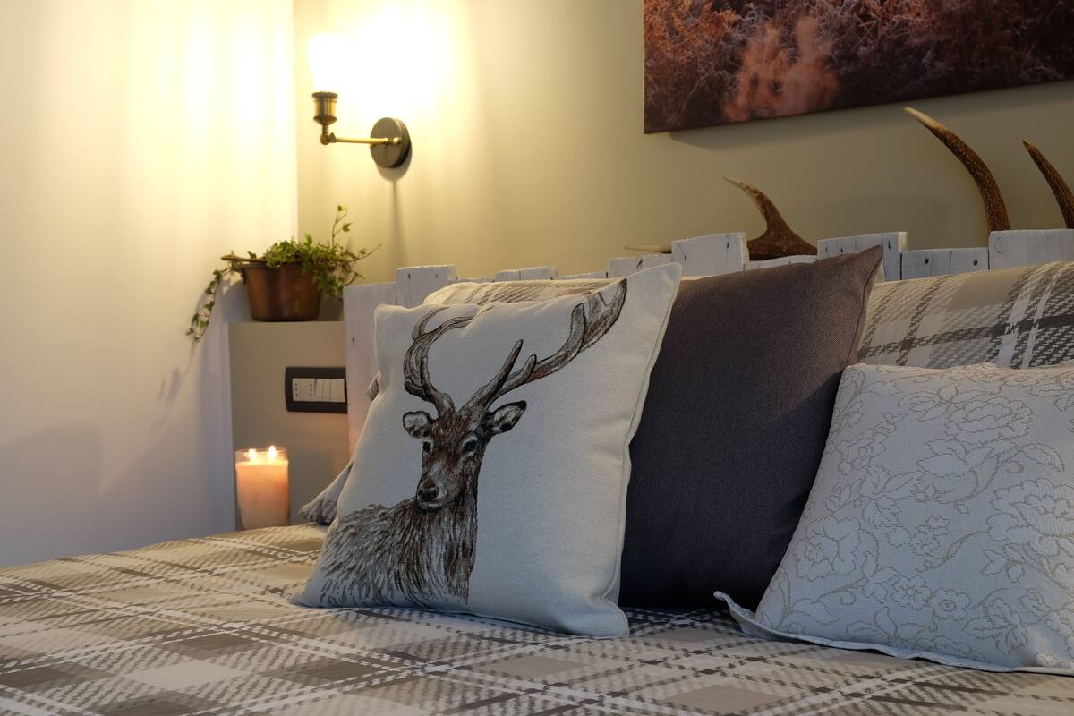 A bed with patterned bedding, decorative pillows, a wall-mounted light, a candle, and a potted plant.