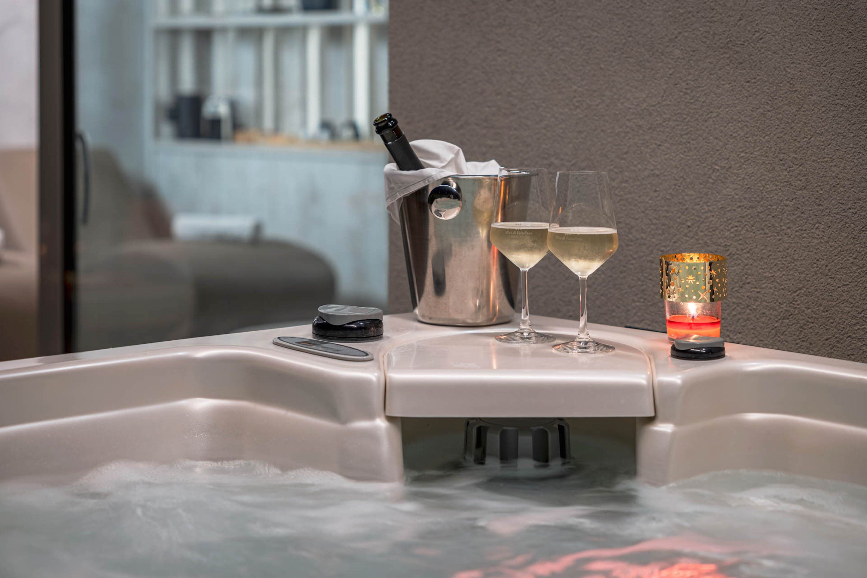 A spa tub with a bottle of champagne, two glasses, and a candle.