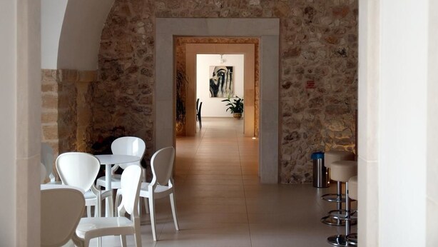 Un arco de piedra que da acceso a un comedor con sillas y mesas blancas.