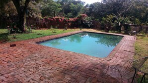 Una piscina rectangular con borde de ladrillo, rodeada de césped y árboles.