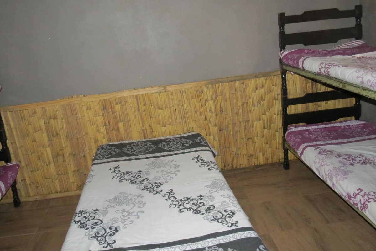 A single bed with a patterned bedspread, a wooden headboard, and a bamboo wall panel.
