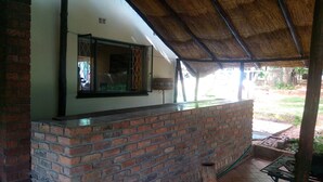 Una barra de ladrillo con ventanal, techo de paja y vistas a un jardín.