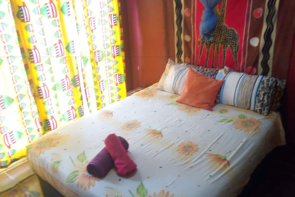 A bed with floral bedding, a teddy bear, and a colorful curtain.