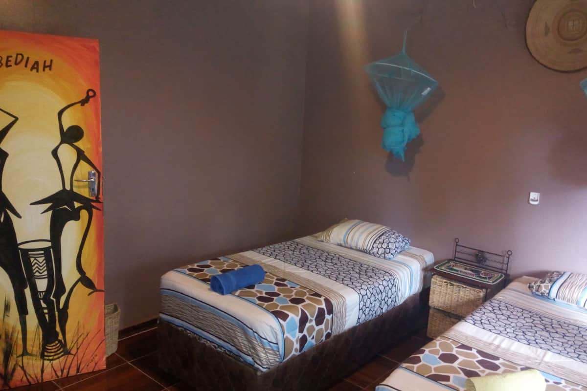 A bedroom with two beds, a wall painting, and mosquito nets.