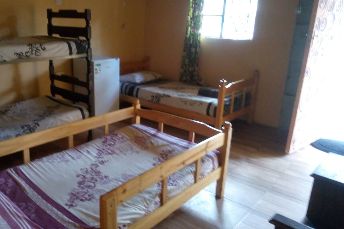 A dormitory room with bunk beds, a wooden desk, and a window with curtains.