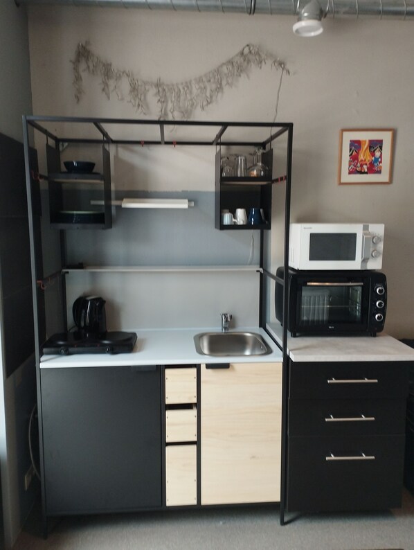 A compact kitchenette with a microwave, kettle, and a sink.