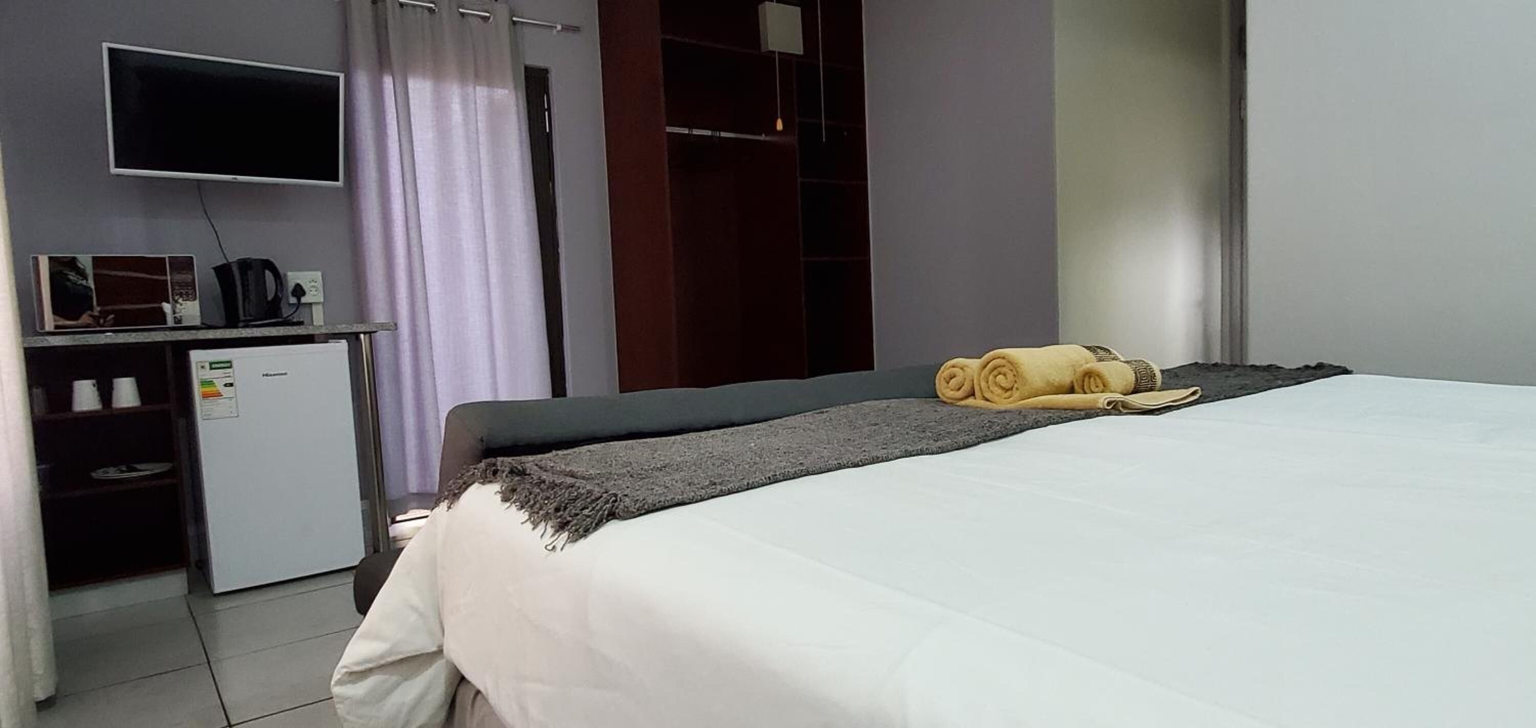 A hotel room with a bed, a desk with a computer, a TV, and a wardrobe.