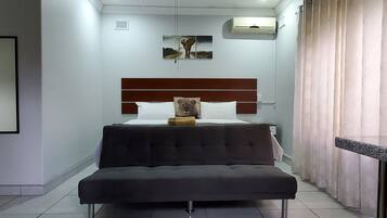 A bedroom with a bed, a bench, a wall-mounted air conditioner, and a window with curtains.