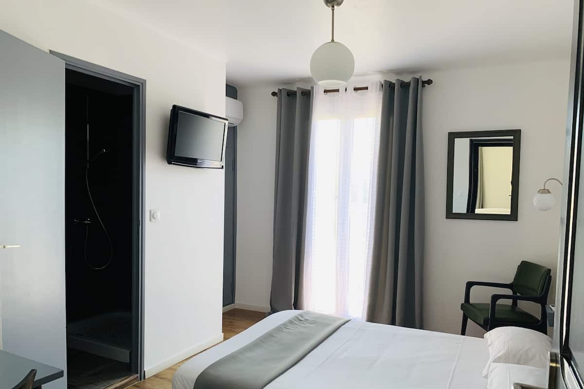 Une chambre d’hôtel équipée d’un lit, d’un téléviseur fixé au mur, d’une chaise et d’un espace douche.