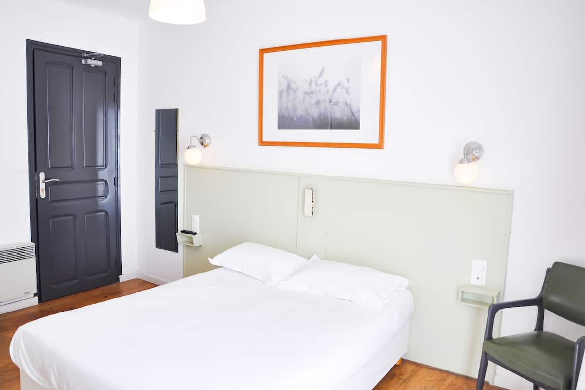 Une chambre à coucher avec un lit, une chaise, une porte et un luminaire fixé au mur.