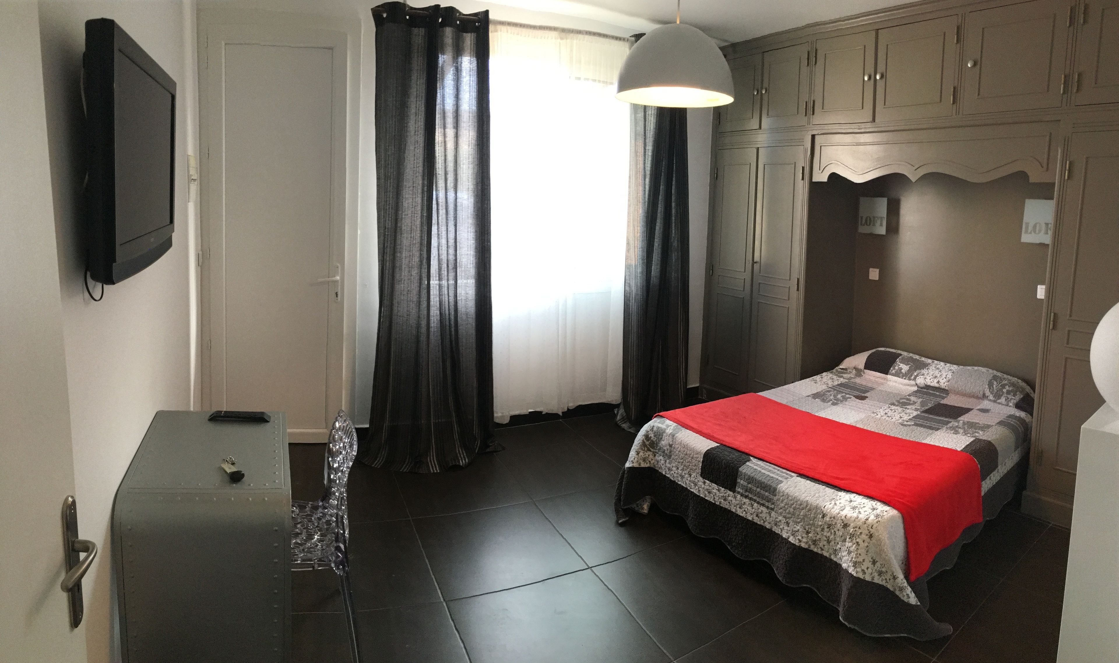 A bedroom with a bed, a desk, a chair, a wardrobe, and a television on the wall.