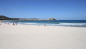 Una playa con cielos despejados, aguas tranquilas y una colina distante.